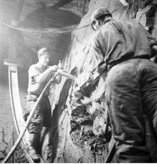 Korytarz prowadzący do komory rozjazdowej. Widoczni górnicy, którzy przy pomocy ręcznych młotów pneumatycznych odspajają ił. 1956 r. Fot. Narodowe Archiwum Cyfrowe